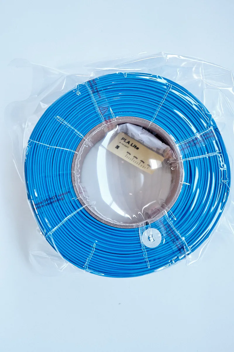 Top view of a vacuum-sealed Bambu Lab PLA Lite Blue 1kg filament refill with a visible silica gel packet and RFID tag.