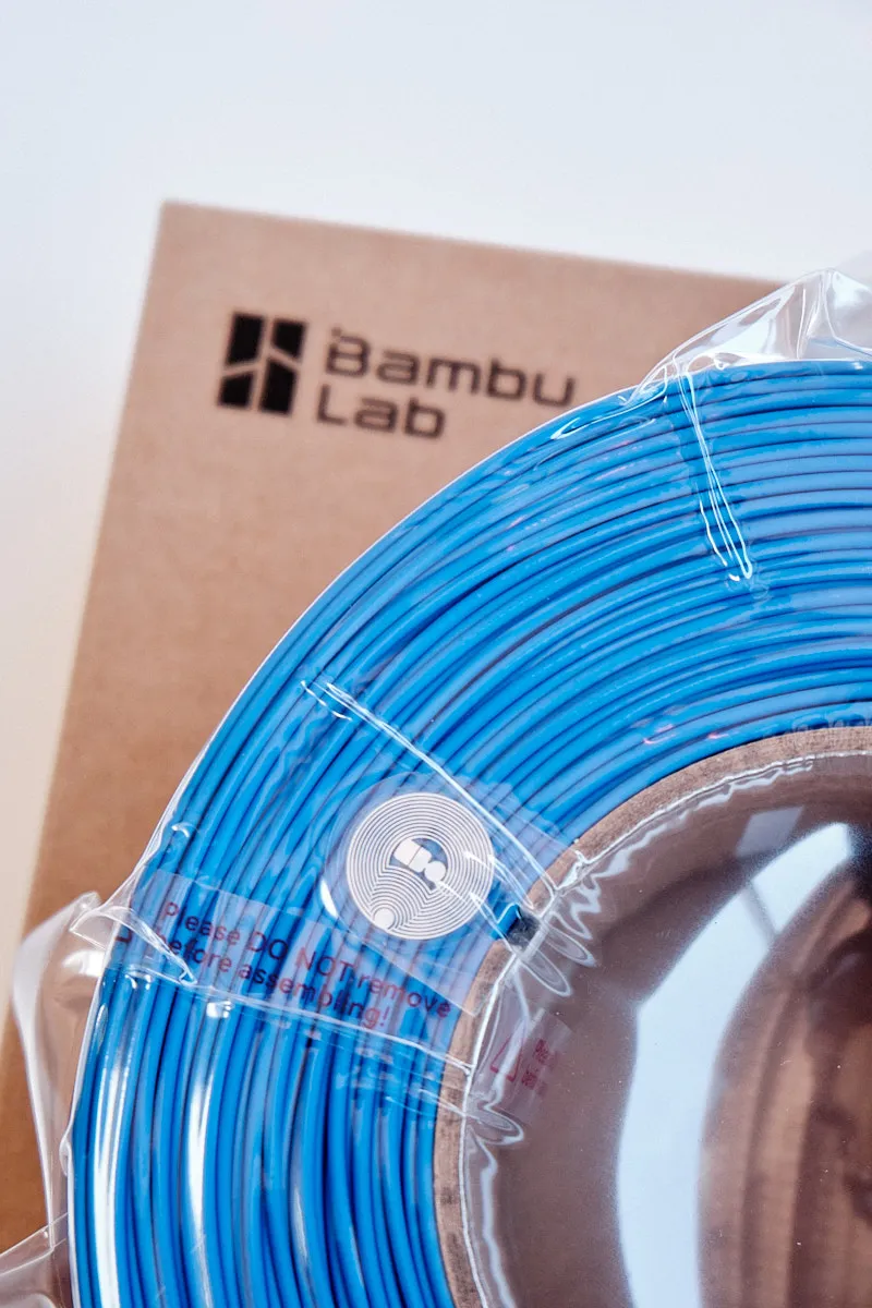 Close-up of Bambu Lab PLA Lite Blue filament showing the integrated RFID tag for automatic material recognition by AMS.