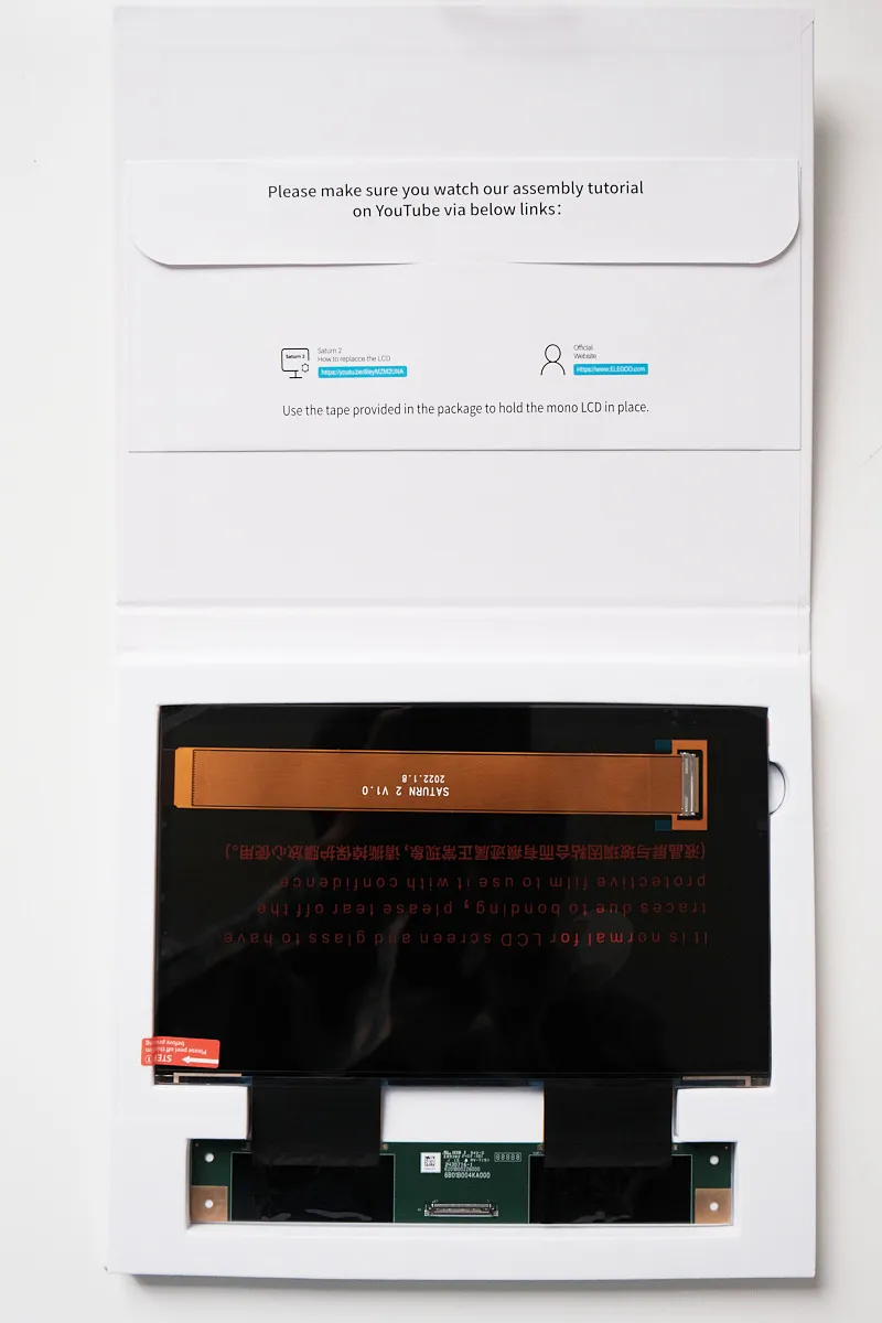Top-down view of the Elegoo Monochrome 8K LCD screen for Saturn 2 / 8K, showing printed user instructions on the box and the LCD screen with attached ribbon cable underneath