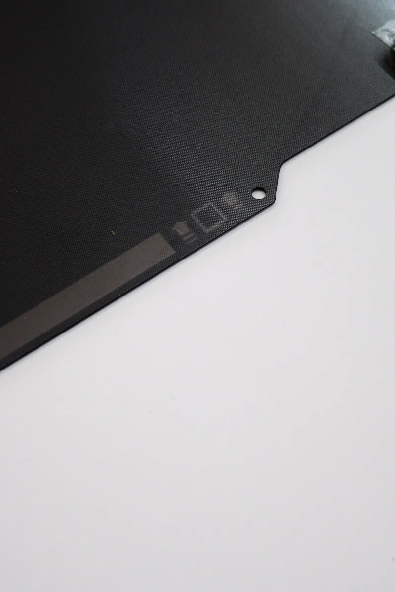 Close-up of the bottom edge of a Bambu smooth PEI build plate, showing printed markings that indicate the direction for lifting and removing the plate