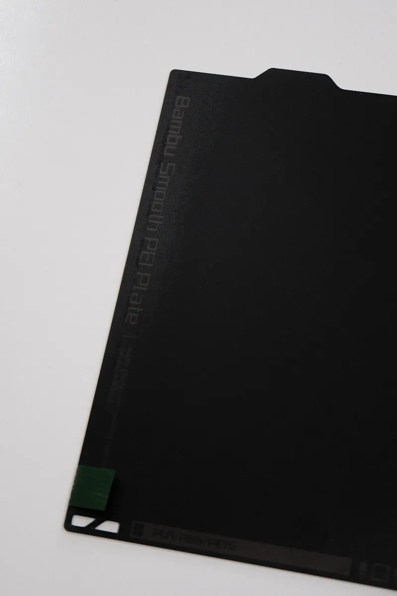 View of the left three-quarters of a Bambu smooth PEI build plate, with printed text “Bambu Smooth PEI Build Plate” near the left edge and material compatibility listed as “PLA / ABS / PETG” along the bottom edge
