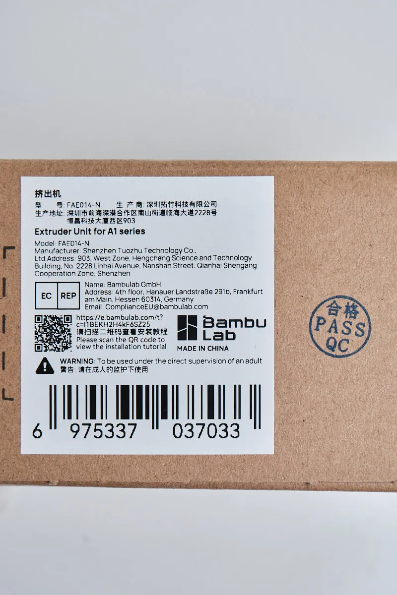 Official product label for Bambu Lab A1 Extruder Unit FAE-014-N showing manufacturer details, barcodes, and QC pass stamp.