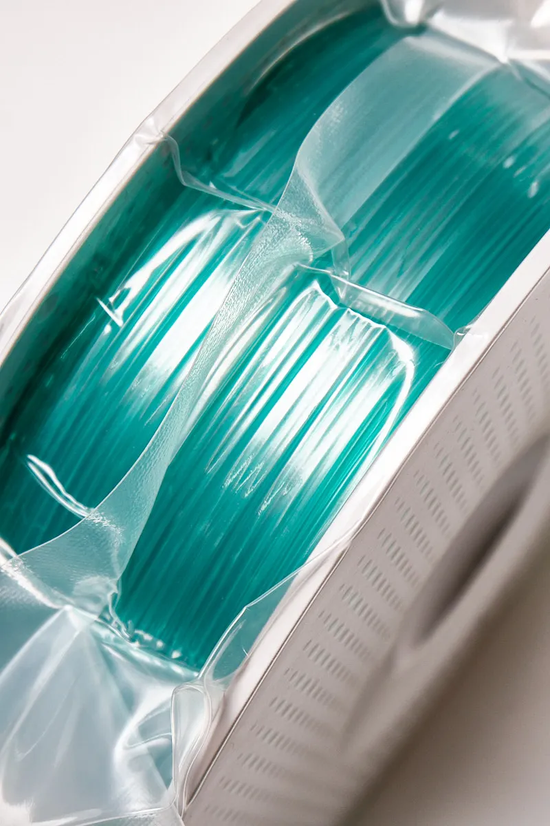 Vacuum-sealed spool of Bambu Lab Translucent Teal PETG 3D printing filament showing the vibrant teal color and translucent texture.