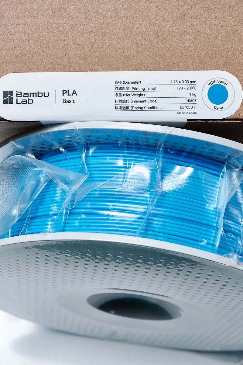 Bambu Lab PLA Basic Cyan 3D printing filament showing specification label with diameter, printing temp, and net weight.
