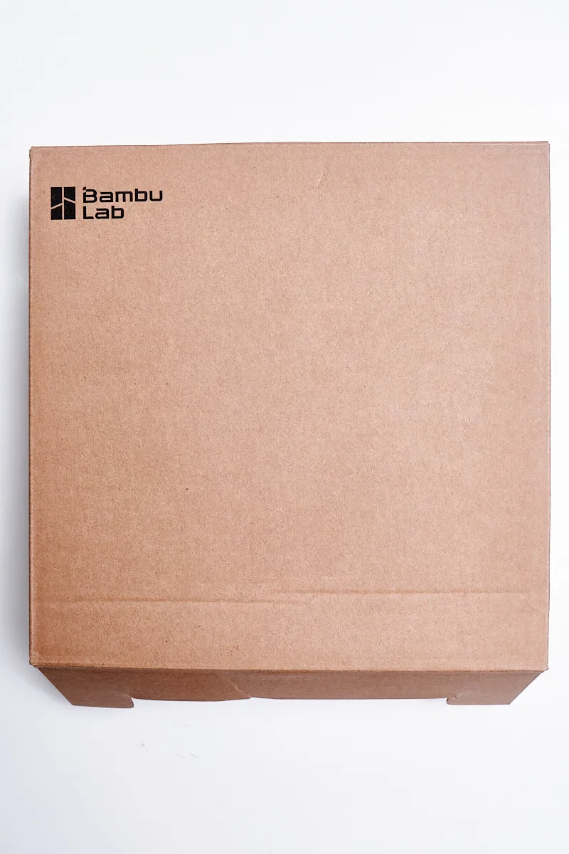 Front view of a square brown cardboard retail box for Bambu Lab 3D printing filament, featuring the black Bambu Lab logo in the top left corner.