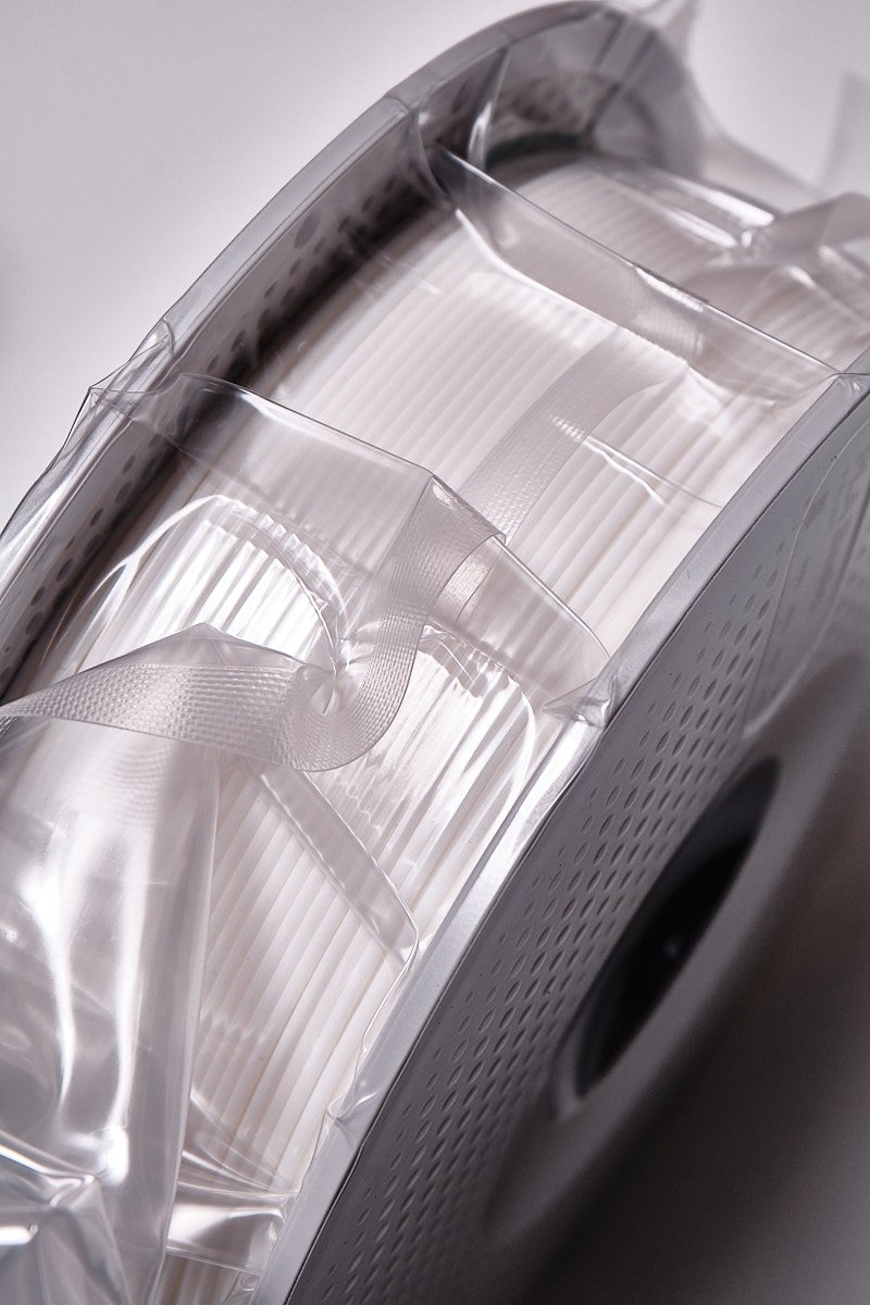 Macro view of neatly wound Jade White PLA Basic filament from Bambu Lab under transparent vacuum seal.