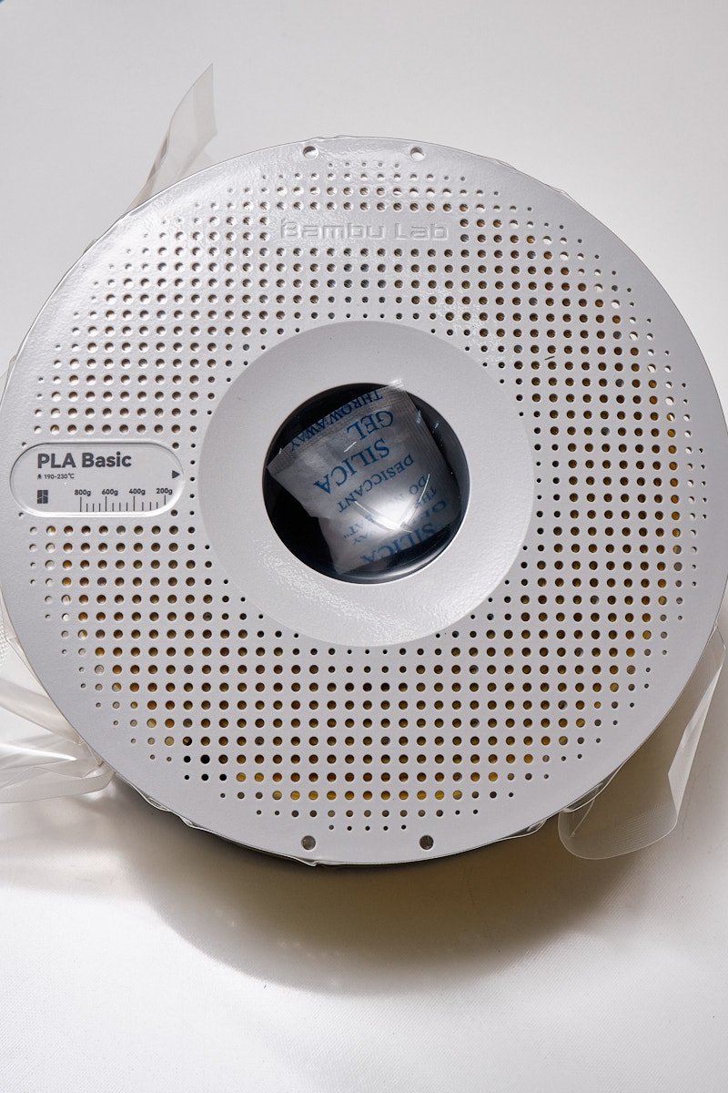 Top view of a Bambu Lab PLA Basic Yellow 1.75mm 3D printing filament spool in original vacuum packaging with silica gel desiccant.