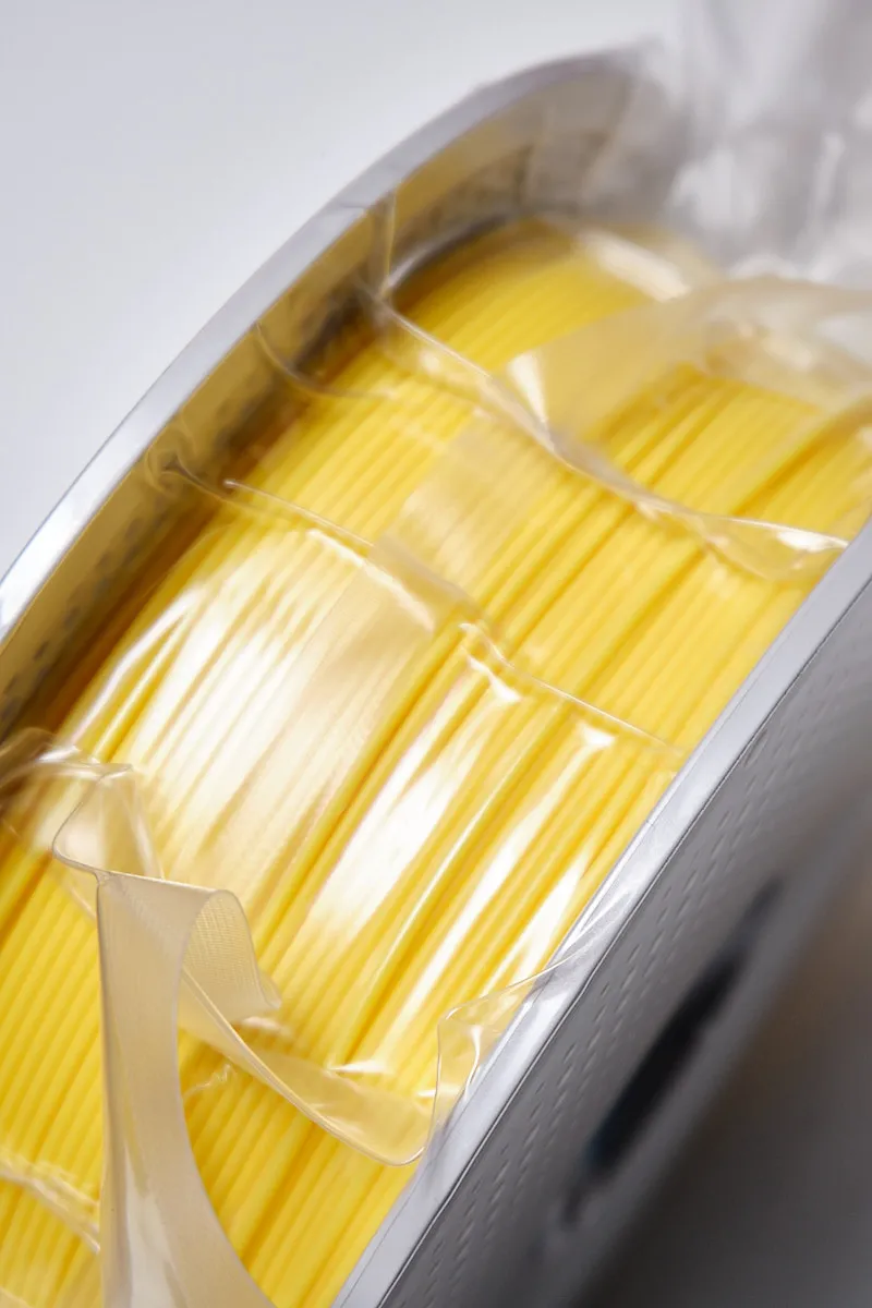 Side view of Bambu Lab PLA Basic Yellow 1.75mm filament showing neat winding and white perforated spool details.