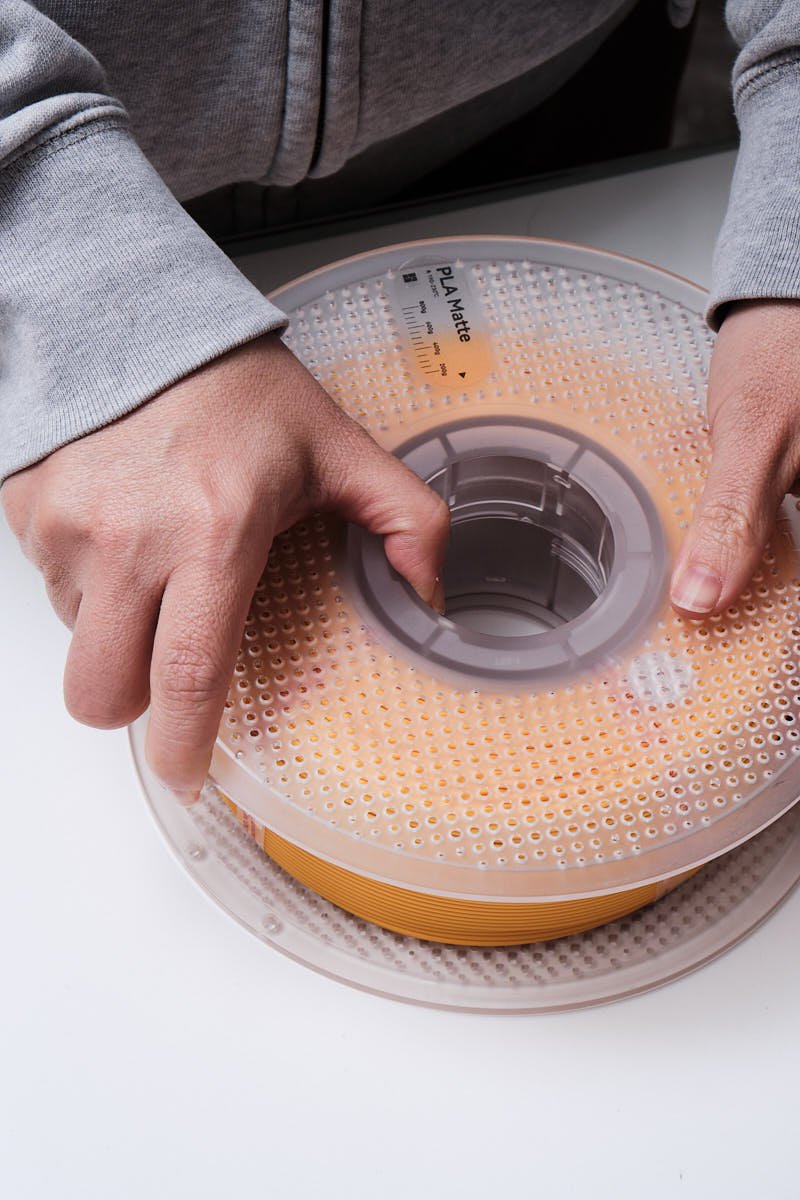 Hands pressing and rotating the two halves of a Bambu Lab reusable spool to lock a Sunflower Yellow PLA Matte filament refill in place.