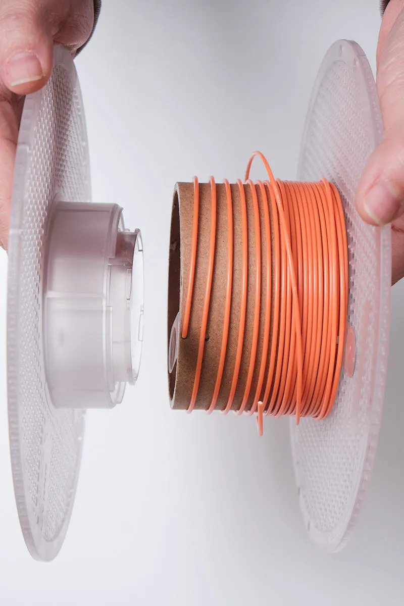 Opening a Bambu Lab reusable spool to remove or replace the Sunflower Yellow PLA filament, showing the two parts of the spool being pulled apart from the cardboard core.
