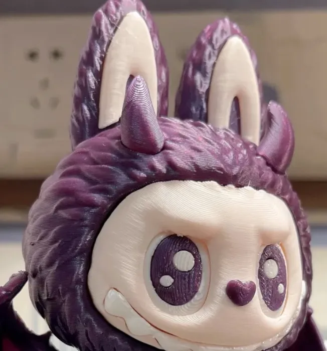 Close-up of a 3D printed character head using Bambu Lab PLA Galaxy Purple filament 13602, showing fine galaxy glitter texture and smooth surface finish