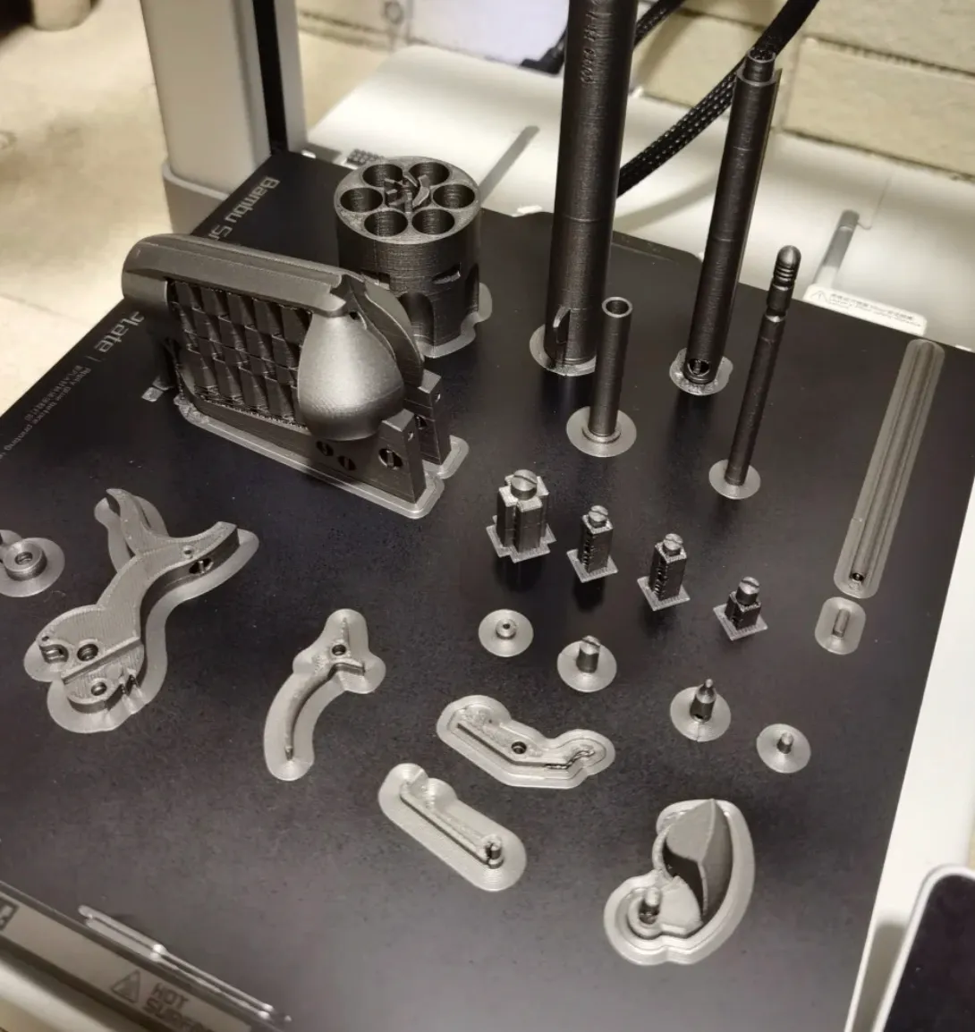 Functional mechanical parts printed with Bambu PLA Metal Iron Gray metallic filament 13100, showing smooth metallic surface finish and dimensional accuracy on a Bambu Lab printer build plate