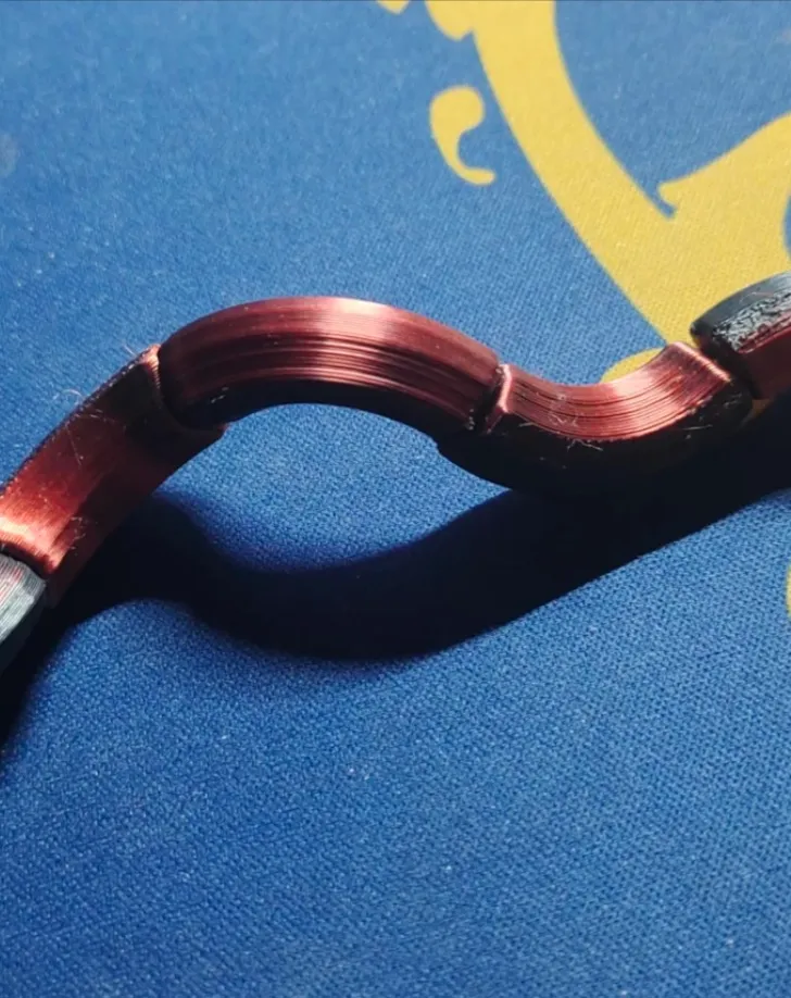 Close-up of Bambu PLA Silk Velvet Eclipse filament showing smooth layered curves with red-to-black velvet metallic sheen