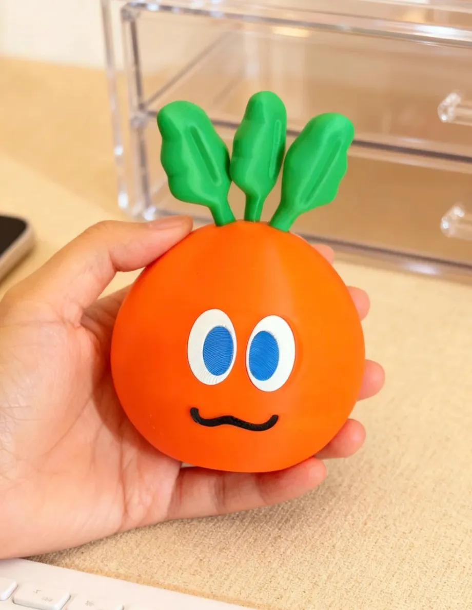 This image shows a hand-held cartoon-style orange-shaped object 3D printed using Bambu Lab PLA Basic Orange filament (10300), with green top details and printed facial features. The surface appears smooth with consistent layer lines.