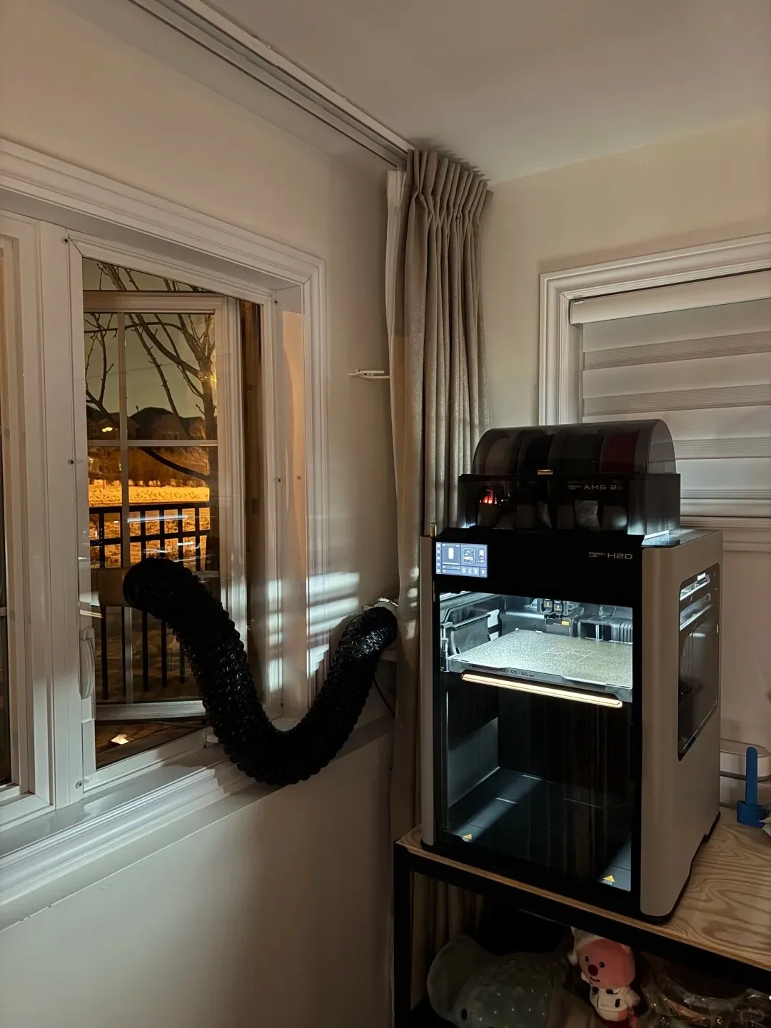 Enclosed Bambu Lab H2D 3D printer with external exhaust duct venting filament fumes out of a window