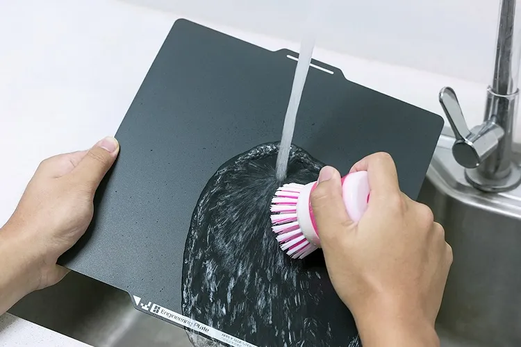 Cleaning the Bambu Engineering build plate under running water using a soft brush