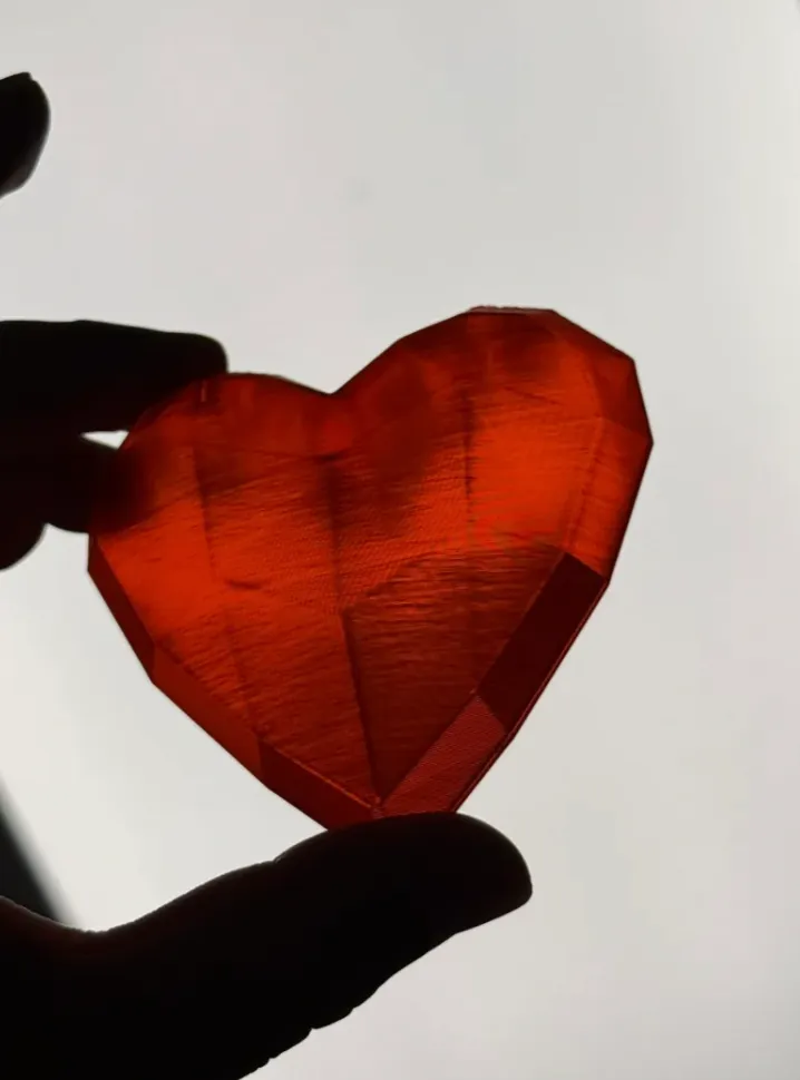 Translucent red heart-shaped 3D print made with Bambu Lab Translucent Red PLA filament 13210, showing strong light transmission and visible layer structure