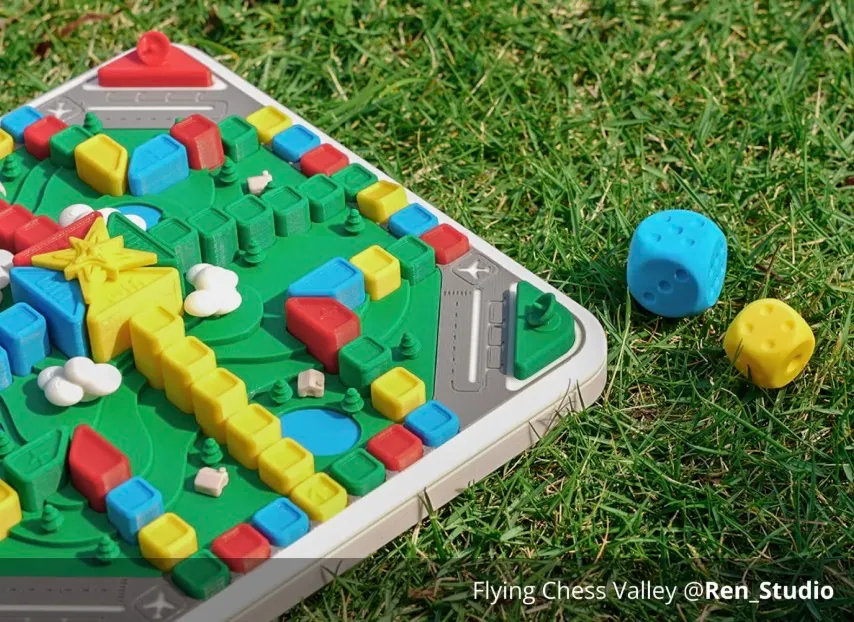 Colorful board game pieces and dice 3D printed using PLA Basic filament on grass background