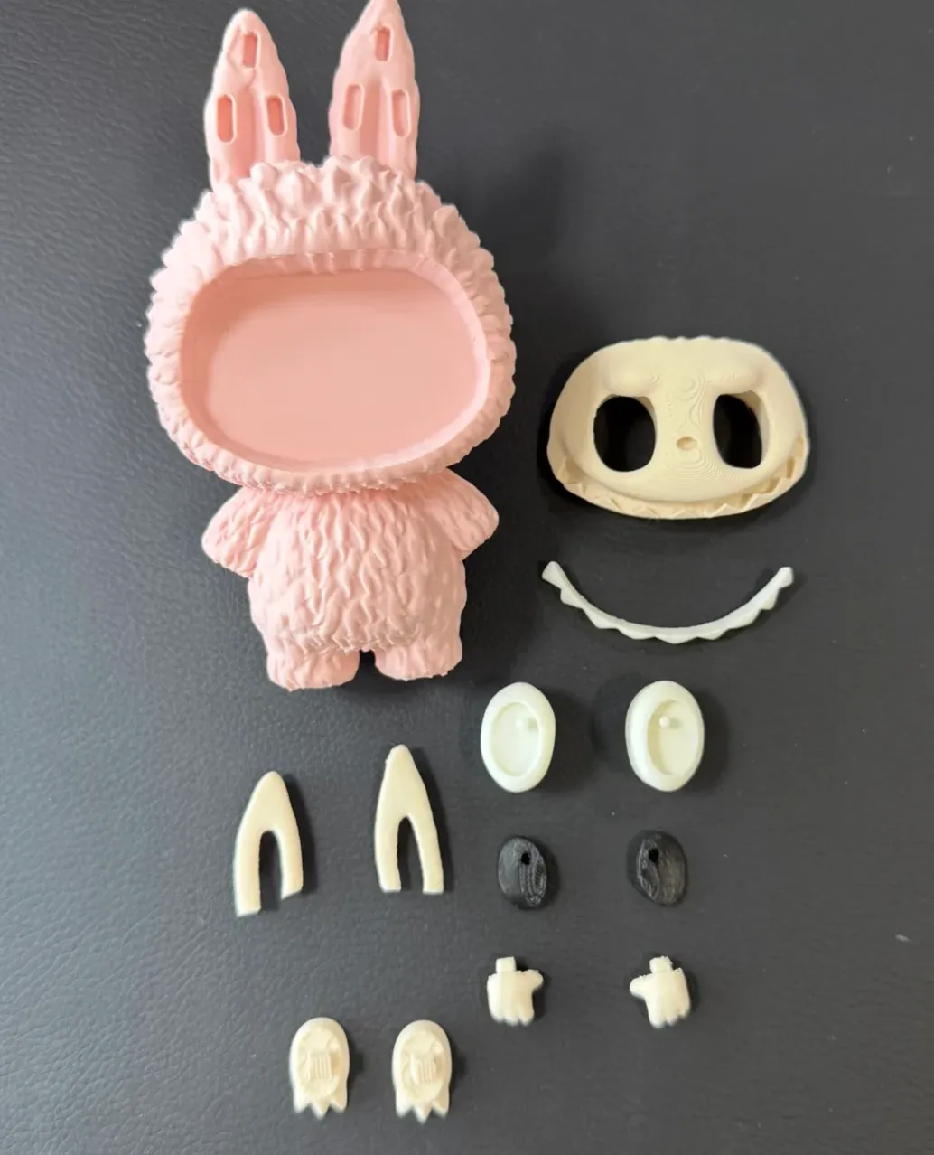 Disassembled 3D printed character parts in soft sakura pink with detailed texture and separate face components