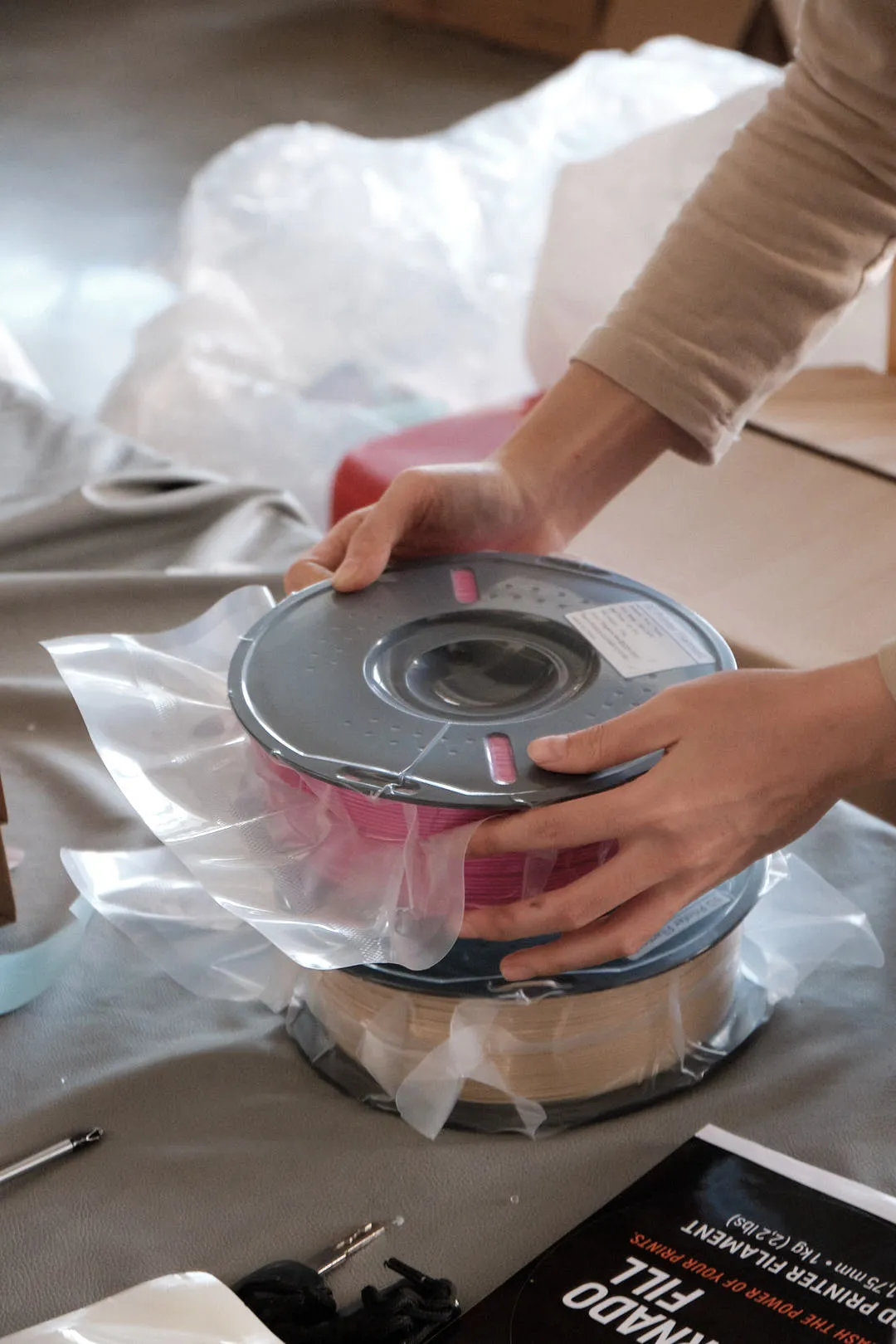 Worker holding a vacuum-sealed 3D printing filament spool during post-packaging handling
