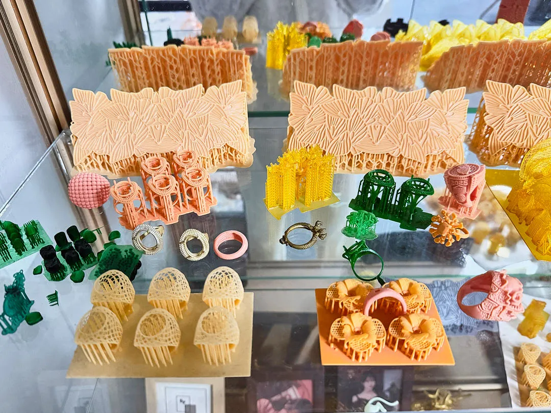 Various resin 3D printed models and jewelry prototypes displayed on glass shelf after UV curing