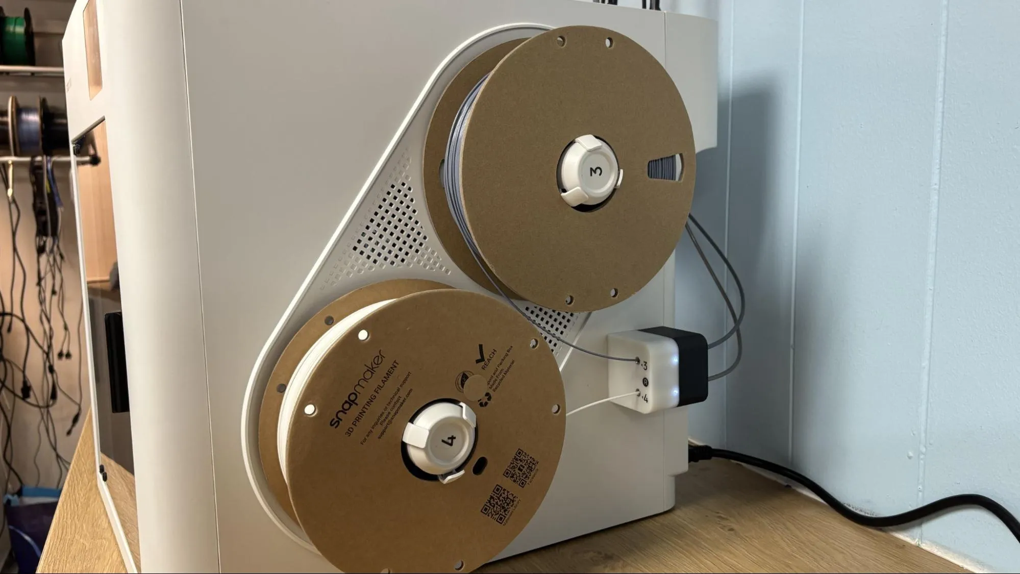Snapmaker U1 3D printer side view showing dual filament spools connected to multi-channel routing module