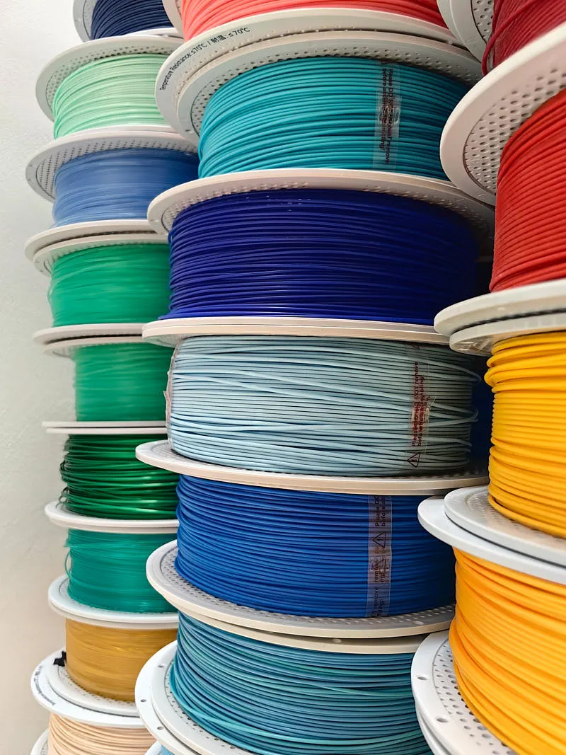 Close-up of stacked 3D printer filament spools in blue, green, yellow and red PLA materials