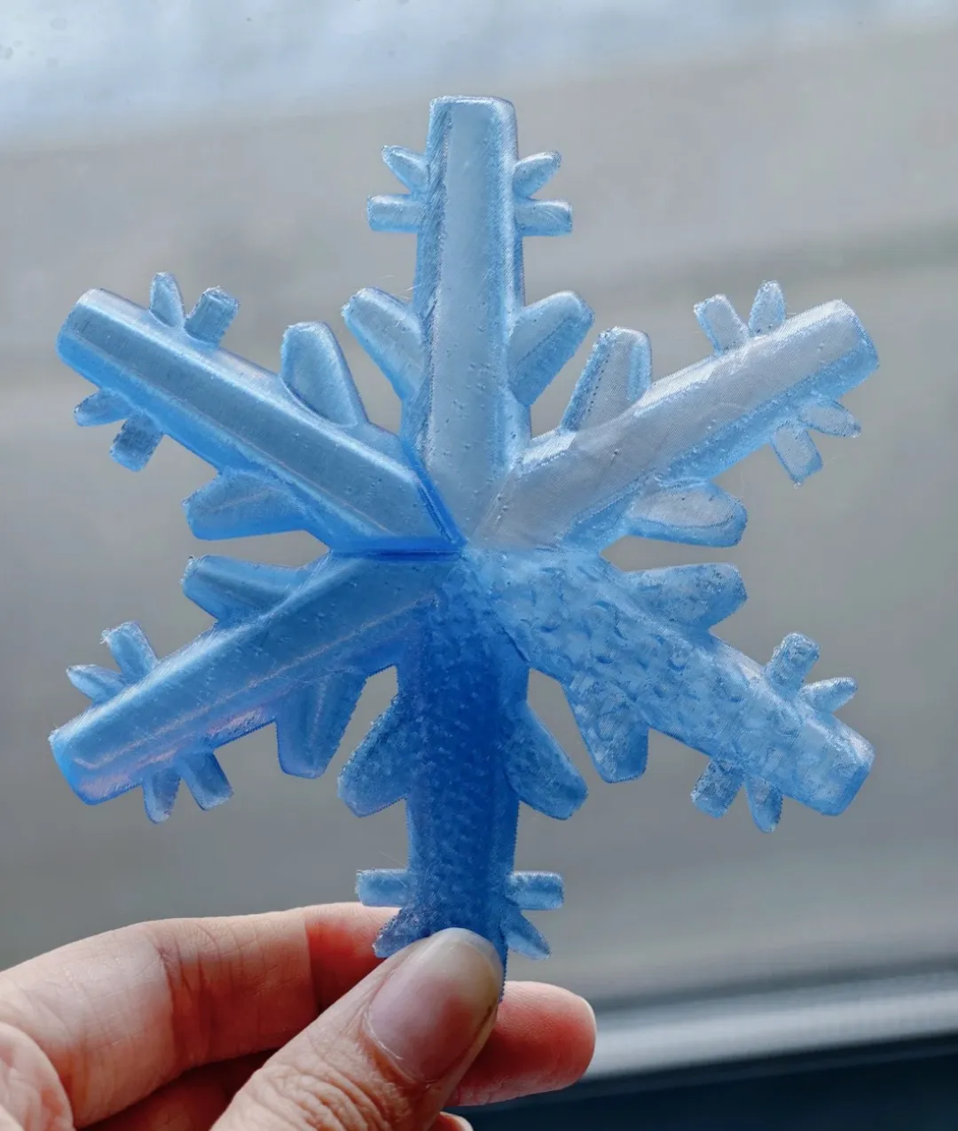 Hand-held snowflake printed with Bambu Lab PETG Translucent Light Blue Filament Color Code 32600 highlighting fine layer lines and translucent finish.