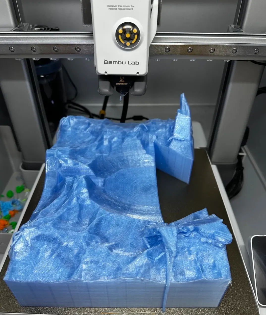 Large terrain model being printed on a Bambu Lab printer using Bambu Lab PETG Translucent Light Blue Filament Color Code 32600, showing translucent blue layer stacking.