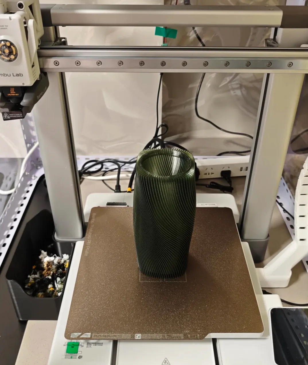 Twisted cylindrical lamp model printed on Bambu Lab build plate using Bambu Lab PETG Translucent Olive Green Filament Color Code 32500.