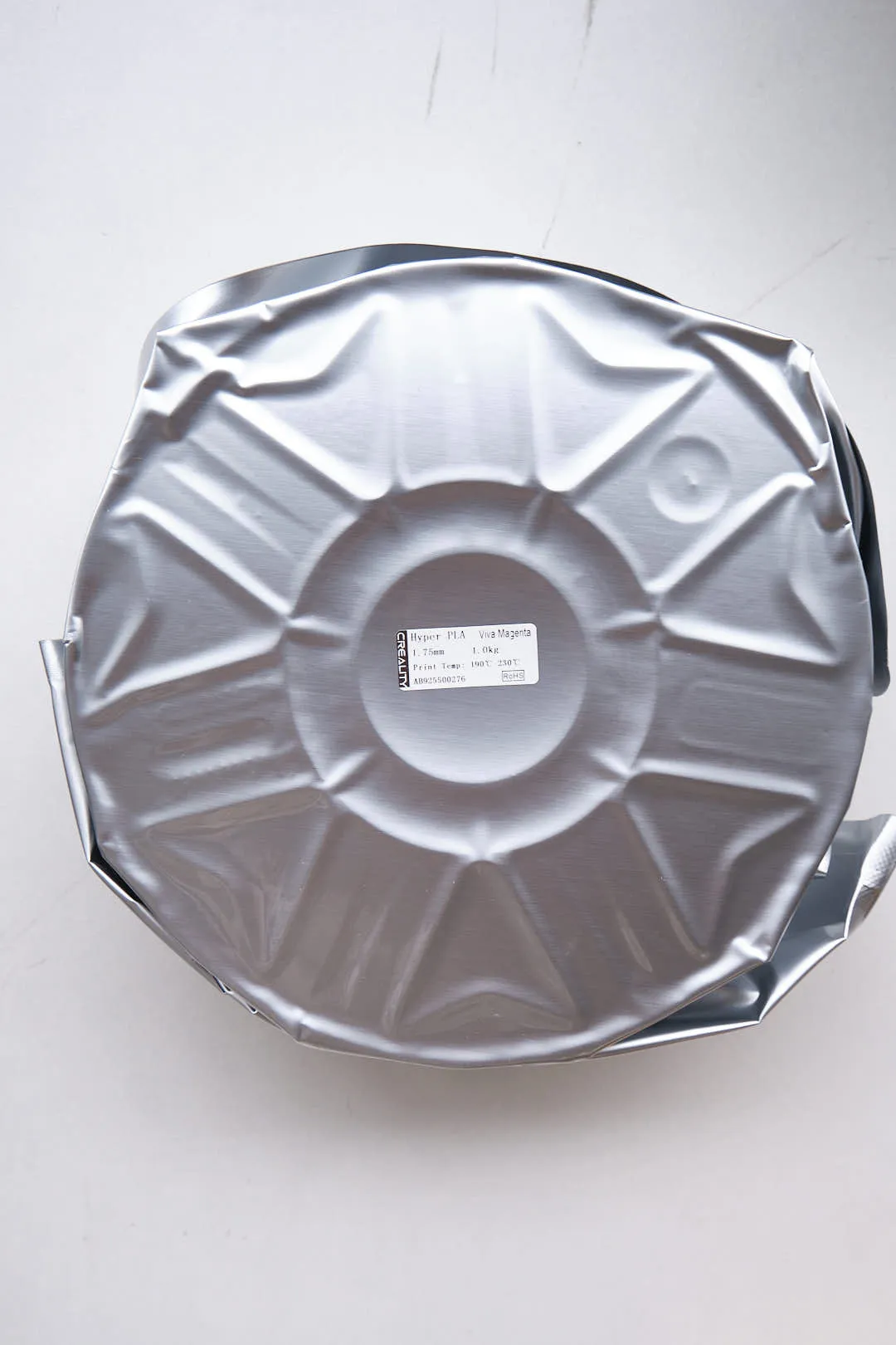 Top view of Creality Hyper PLA RFID Viva Magenta filament sealed in vacuum foil packaging showing spool shape underneath