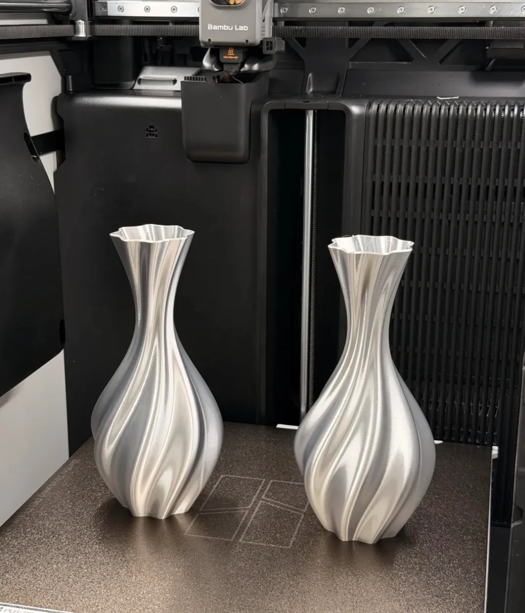 Two decorative vases printed on 3D printer build plate using Bambu Lab PLA Silk+ Silver Filament 1.75mm 1kg/Spool Color Code 13109 with metallic silk finish
