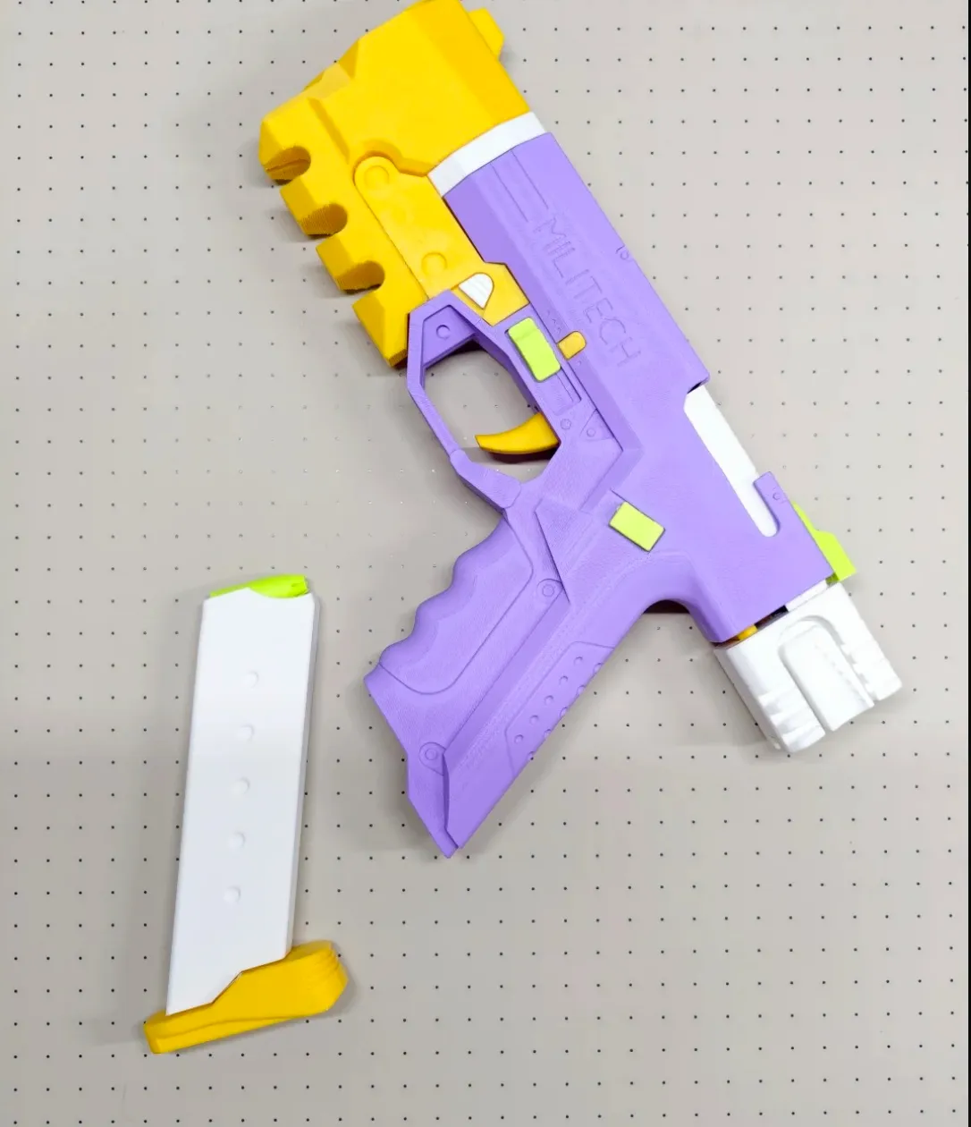 3D printed toy blaster in matte lilac purple with yellow and white components displayed on pegboard surface