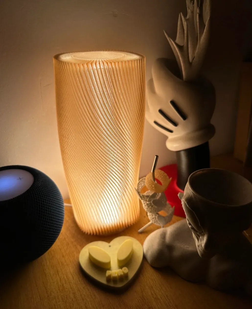 Spiral lamp shade printed with Bambu Lab PETG Translucent Brown Filament Color Code 32800 glowing warmly under internal lighting on a bedside table.