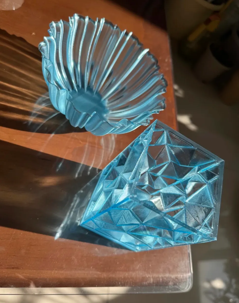 Decorative bowl and geometric crystal model printed with Bambu Lab PETG Translucent Light Blue Filament Color Code 32600 under natural light.