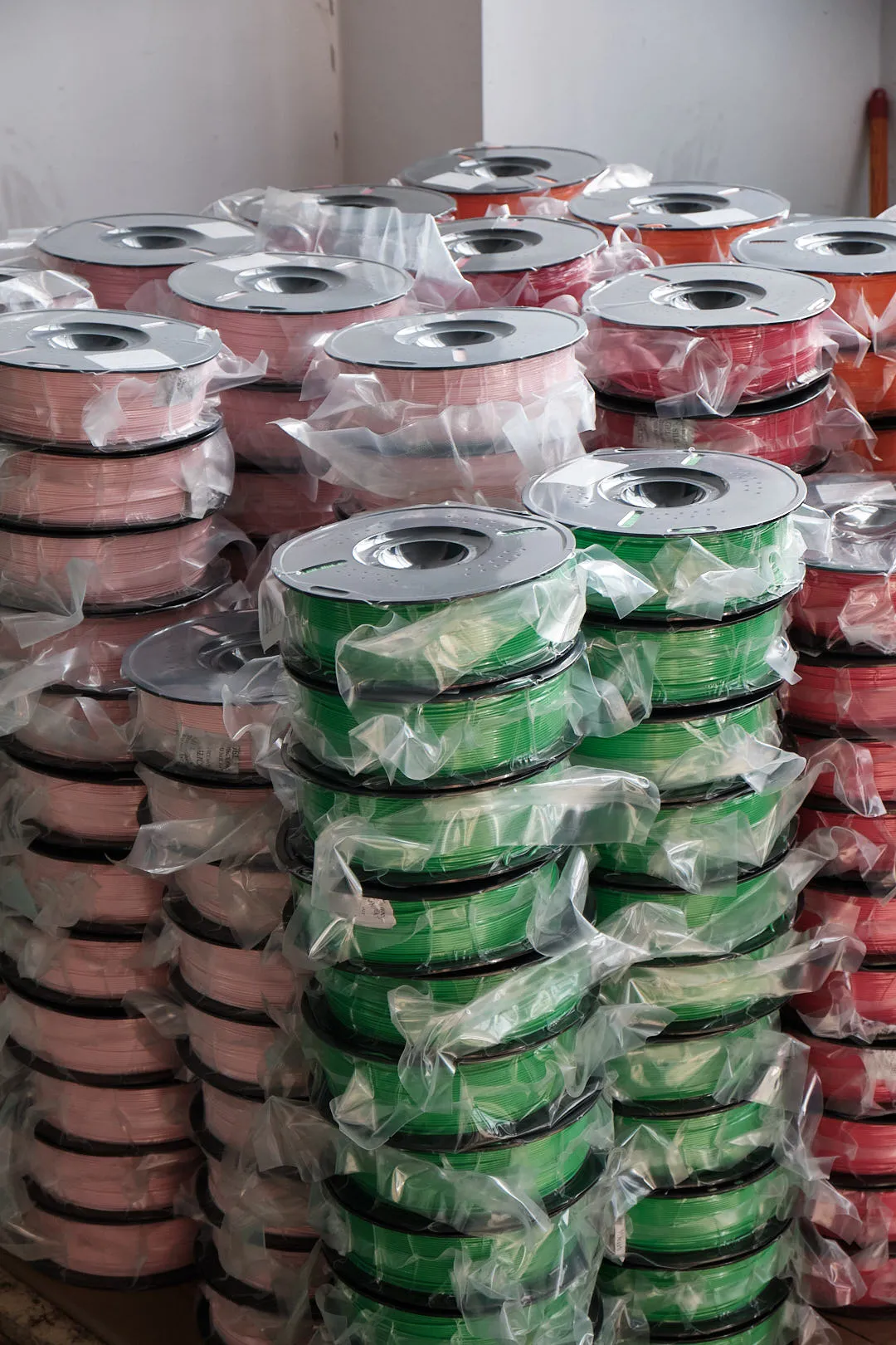 stacked 3D printing filament spools vacuum sealed in plastic bags green pink red bulk filament storage