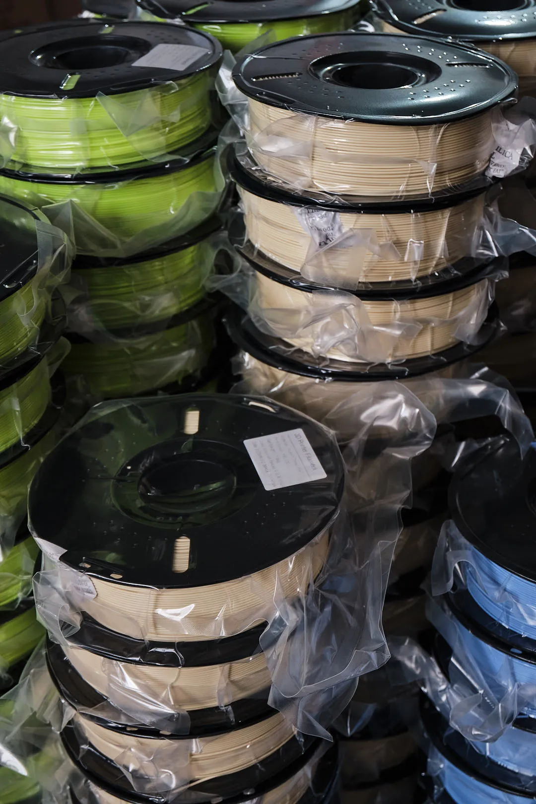 stacked 3d printing filament spools vacuum sealed packaging green beige blue colors warehouse storage