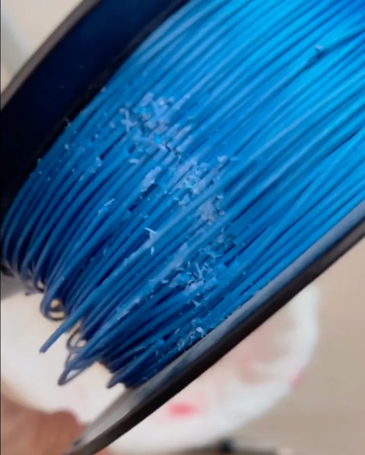 blue PLA filament on spool showing surface residue flakes and rough texture from degradation