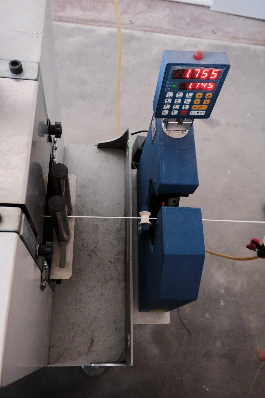 3D printing filament passing through a digital diameter measurement device showing real-time readings