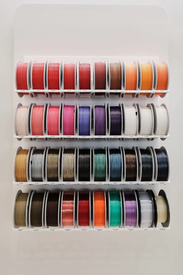 filament display shelf with labeled 3d printing materials in yellow green gray black and multicolor spools