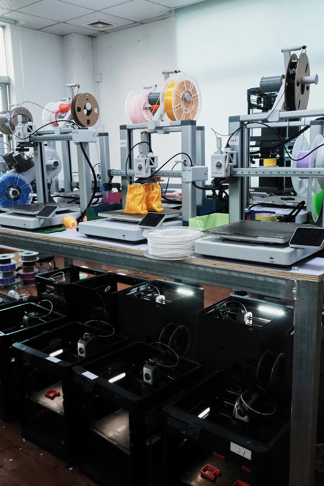 row of desktop 3D printers using various filament spools in a printing workshop
