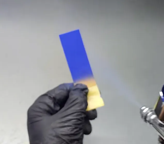hand holding rectangular test strip while spray painting gradient color with spray gun